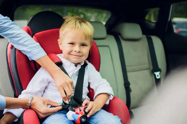 Bébé garçon avec des cheveux bouclés assis dans le siège auto enfant avec voiture jouet dans les mains — Photo