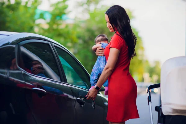 Une femme avec un bébé dans les bras, se tient près de la voiture et veut ouvrir la porte. concept de situation complexe — Photo