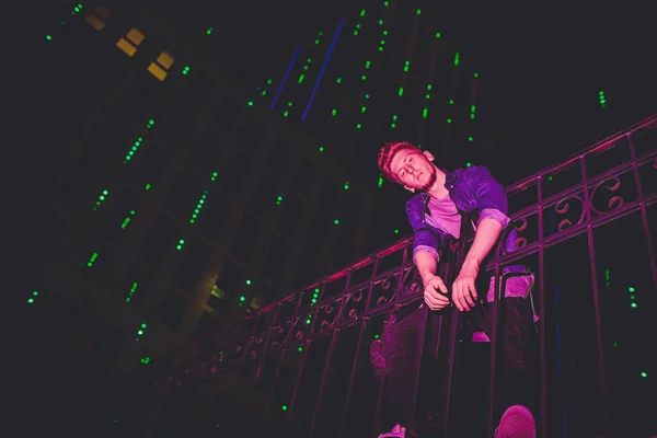 Joven hombre pelirrojo sobre fondo negro nocturno. luces de la ciudad nocturna. en el modelo cae la luz de la publicidad al aire libre — Foto de Stock