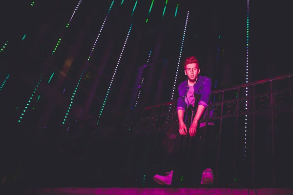 Joven hombre pelirrojo sobre fondo negro nocturno. luces de la ciudad nocturna. en el modelo cae la luz de la publicidad al aire libre —  Fotos de Stock