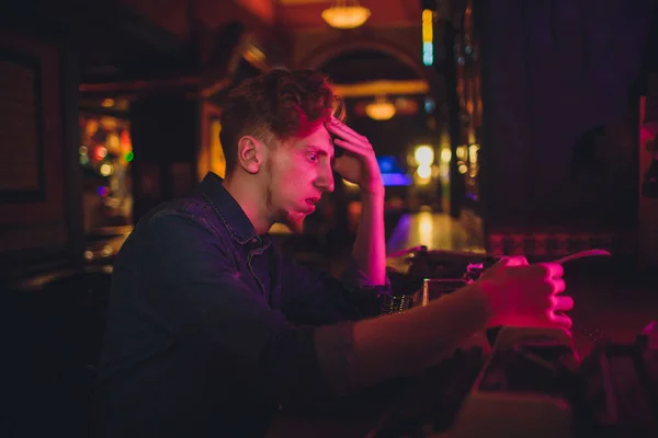 Un joven escribiendo en una vieja máquina de escribir. en iluminación oscura, restaurante, ropa moderna, viejos hábitos de escritor — Foto de Stock