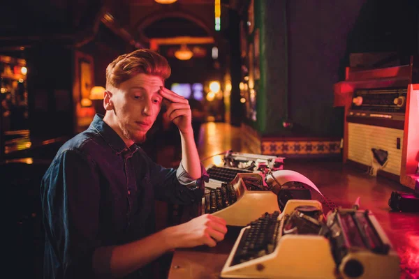 Young man writing on old typewriter. in dark lighting, restaurant, modern clothes, old writer habits