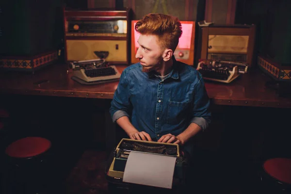 Young man writing on old typewriter. in dark lighting, restaurant, modern clothes, old writer habits