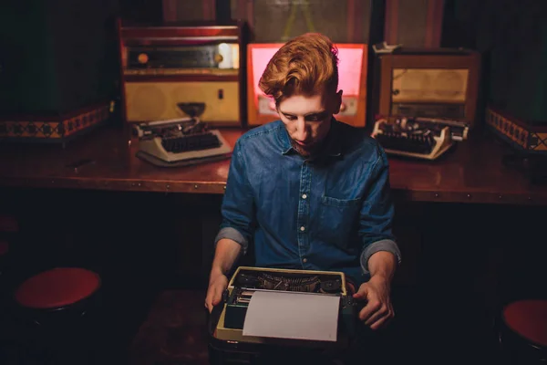 Young man writing on old typewriter. in dark lighting, restaurant, modern clothes, old writer habits