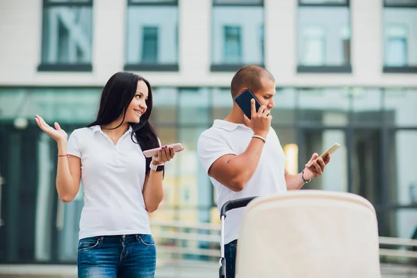 Muž a žena pomocí telefonů. dítě ve vozíku, koncept zaneprázdnění rodiče — Stock fotografie