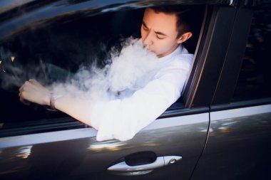 Yan genç adam bir kentsel sokağa arabasını kullanıyor gibi bir e-sigara sigara üzerinden görüntüleyin. araba sürücüsü peeps dışında araba ve sigara