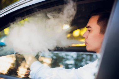 Yan genç adam bir kentsel sokağa arabasını kullanıyor gibi bir e-sigara sigara üzerinden görüntüleyin. araba sürücüsü peeps dışında araba ve sigara