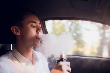 Bir genç adam o kentsel bir sokağa arabasını kullanıyor gibi bir e-sigara sigara yan görünümden elektronik sigara açılırsa