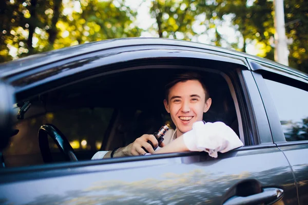 Vista do lado do jovem fumando um cigarro eletrônico enquanto dirige seu carro em uma rua urbana. motorista de carro espreita para fora do carro e fuma — Fotografia de Stock