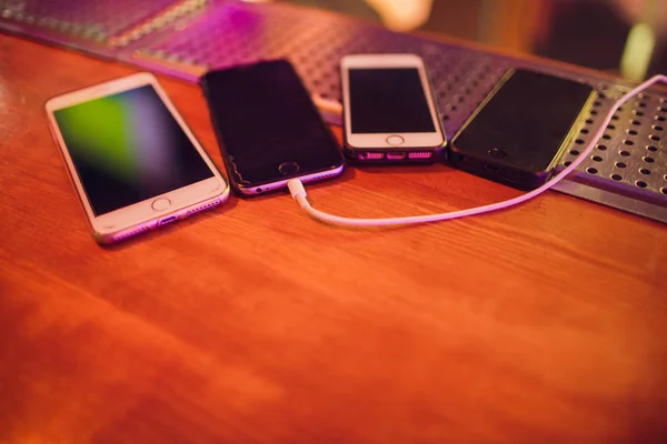 Quatro telefones no bar do clube. um smartphone está carregando. outros telefones à espera de sua vez - carregamento — Fotografia de Stock