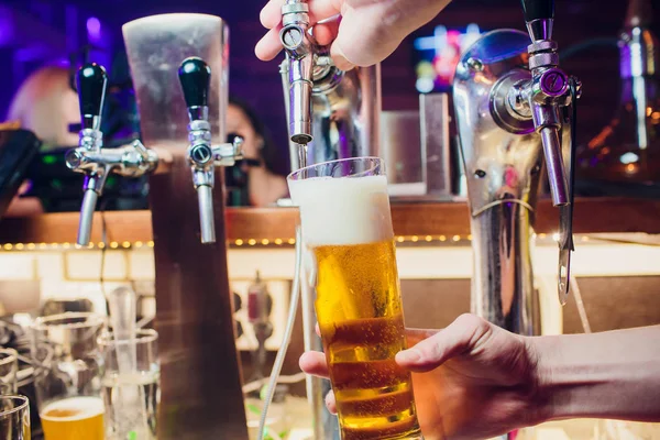 Eine junge Frau spendet Bier in einer Bar aus Metallzapfen. Schöne Barkeeperin zapft Bier in Bar. — Stockfoto