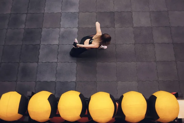 Bovenaanzicht van een fit en sportief meisje doet streching oefeningen voor de benen. Jonge slanke vrouw doen bindgaren in de sportschool, stadion. Binnenshuis. — Stockfoto