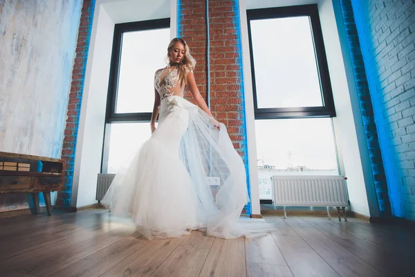 Schöne blonde Frau mit langen Haaren trägt Kleid mit nackten Schultern und posiert am Fenster. — Stockfoto