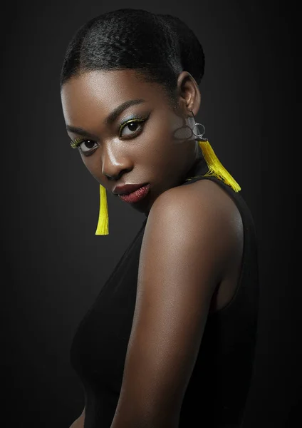 Close-up portrait of beautiful afro woman with make-up. with yellow earrings on a black background — Stock Photo, Image