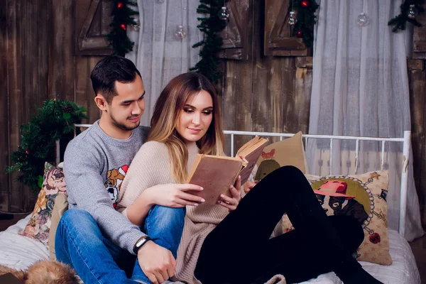 Pasando un buen rato en casa. Hermosa joven pareja amorosa que se une entre sí y sonríe mientras la mujer sostiene un libro . —  Fotos de Stock