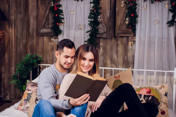 Passer du bon temps à la maison. Beau jeune couple aimant coller les uns aux autres et souriant tandis que la femme tenant un livre . — Photo