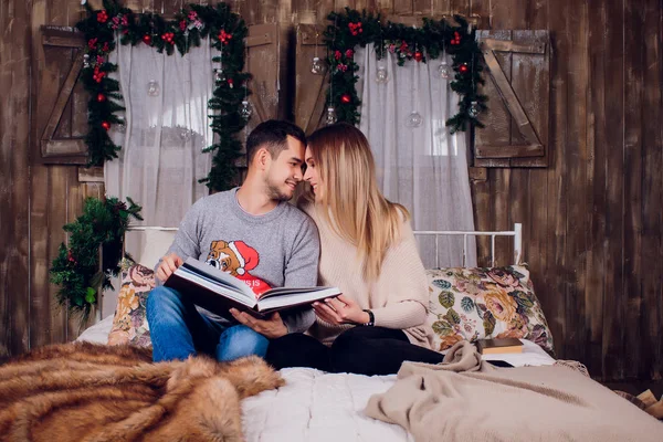 Pasando un buen rato en casa. Hermosa joven pareja amorosa que se une entre sí y sonríe mientras la mujer sostiene un libro . —  Fotos de Stock