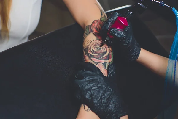 Girl tattoo artist doing a tattoo on her hand, pink typewriter, on a black table. — Stock Photo, Image