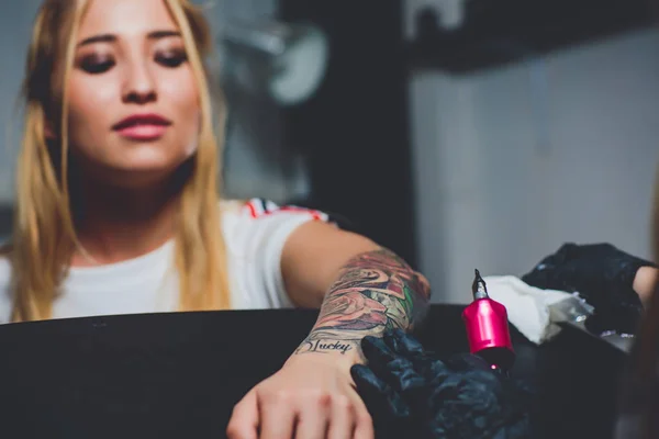 girl tattoo artist doing a tattoo on her hand, pink typewriter, on a black table.