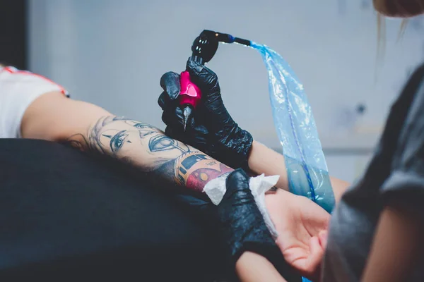 Dziewczyna tatuażysta robi tatuaż na jej dłoni, różowy maszyny do pisania, na stół czarny. — Zdjęcie stockowe