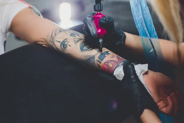 Dziewczyna tatuażysta robi tatuaż na jej dłoni, różowy maszyny do pisania, na stół czarny. — Zdjęcie stockowe