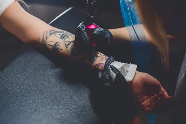 Artista de tatuagem menina fazendo uma tatuagem na mão, máquina de escrever rosa, em uma mesa preta . — Fotografia de Stock