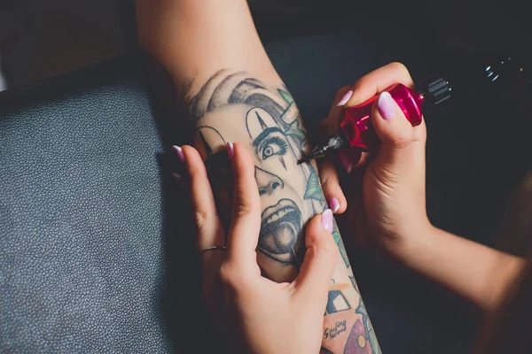黒いテーブルの上の彼女の手、ピンク タイプライターに入れ墨をしている女の子のタトゥー アーティスト. — ストック写真