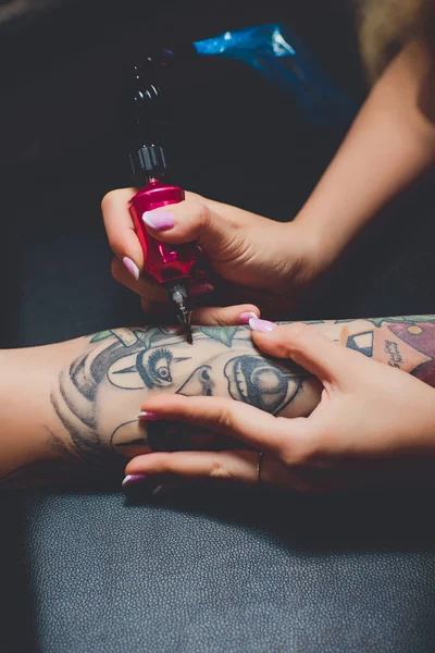 Meisje tatoeëerder doet een tattoo op haar hand, roze typemachine, op een zwarte lijst. — Stockfoto