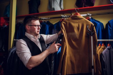 terzi keser ve bir takım elbise diker. Terzilik dükkanı genç bir erkekte erkek giyim yapar. Ismarlama giyim Atölyesi. onun elinde Elektrikli Ütü tutar. ıslak-ısıl işlem