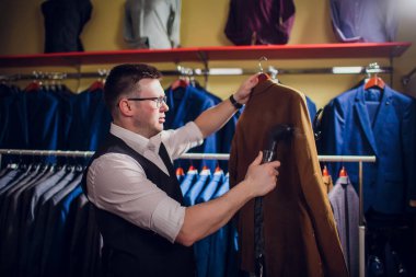 terzi keser ve bir takım elbise diker. Terzilik dükkanı genç bir erkekte erkek giyim yapar. Ismarlama giyim Atölyesi. onun elinde Elektrikli Ütü tutar. ıslak-ısıl işlem