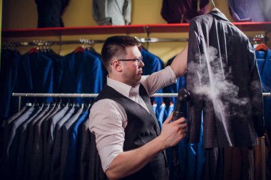 terzi keser ve bir takım elbise diker. Terzilik dükkanı genç bir erkekte erkek giyim yapar. Ismarlama giyim Atölyesi. onun elinde Elektrikli Ütü tutar. ıslak-ısıl işlem