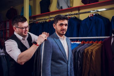 Satır karşı klasik yelek işadamı dükkanda uygun. Adam başka bir takım elbise giyim mağazası denemede yardımcı olur.