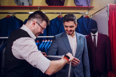 Satır karşı klasik yelek işadamı dükkanda uygun. Adam başka bir takım elbise giyim mağazası denemede yardımcı olur.