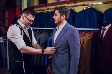 Satır karşı klasik yelek işadamı dükkanda uygun. Adam başka bir takım elbise giyim mağazası denemede yardımcı olur.