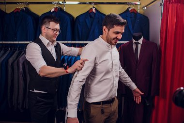 Satır karşı klasik yelek işadamı dükkanda uygun. Adam başka bir takım elbise giyim mağazası denemede yardımcı olur.