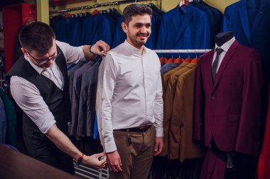 Satır uygun dükkanda karşı klasik yelek'iş adamıdır. Adam bir takım elbise giyim mağazası başka bir denemede yardımcı olur.