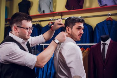 Satır karşı klasik yelek işadamı dükkanda uygun. Adam başka bir takım elbise giyim mağazası denemede yardımcı olur.