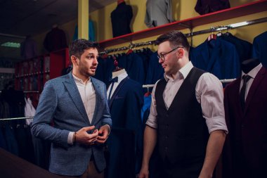 Satır karşı klasik yelek işadamı dükkanda uygun. Adam başka bir takım elbise giyim mağazası denemede yardımcı olur.