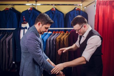 Satır karşı klasik yelek işadamı dükkanda uygun. Adam başka bir takım elbise giyim mağazası denemede yardımcı olur.