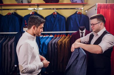 Satır karşı klasik yelek işadamı dükkanda uygun. Adam başka bir takım elbise giyim mağazası denemede yardımcı olur.