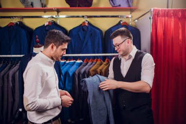 Satır karşı klasik yelek işadamı dükkanda uygun. Adam başka bir takım elbise giyim mağazası denemede yardımcı olur.