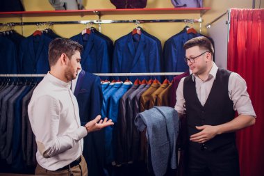 Satır karşı klasik yelek işadamı dükkanda uygun. Adam başka bir takım elbise giyim mağazası denemede yardımcı olur.