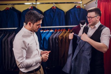 Satır karşı klasik yelek işadamı dükkanda uygun. Adam başka bir takım elbise giyim mağazası denemede yardımcı olur.