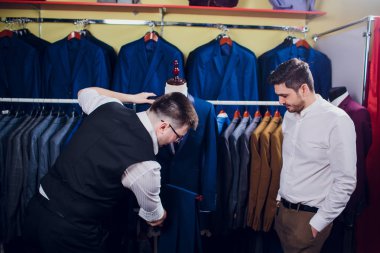 Satır karşı klasik yelek işadamı dükkanda uygun. Adam başka bir takım elbise giyim mağazası denemede yardımcı olur.