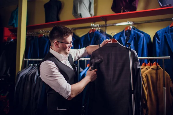 terzi keser ve bir takım elbise diker. Terzilik dükkanı genç bir erkekte erkek giyim yapar. Ismarlama giyim Atölyesi. onun elinde Elektrikli Ütü tutar. ıslak-ısıl işlem