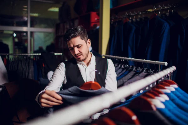 Tailor, tailoring. Mens suit, tailor in his workshop. Elegant mans suits hanging in row. Luxury mens classic suits on rack in elegant mens boutique.