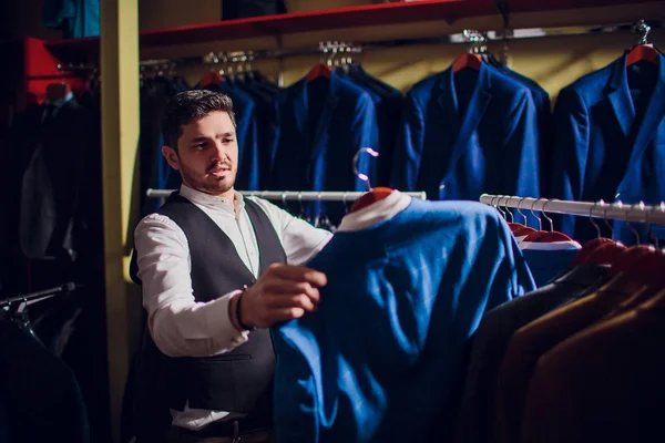 Tailor, tailoring. Mens suit, tailor in his workshop. Elegant mans suits hanging in row. Luxury mens classic suits on rack in elegant mens boutique.