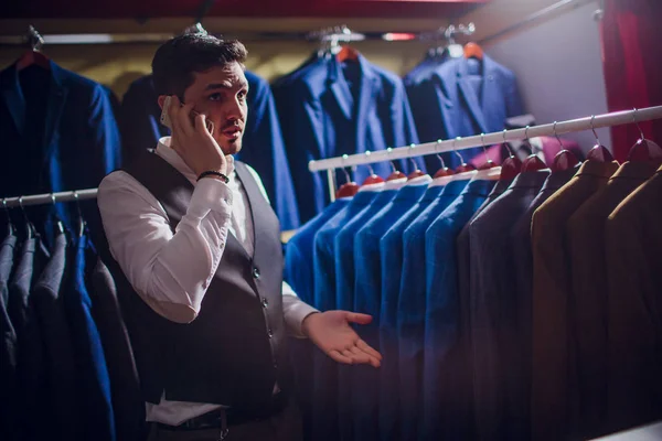 Πώληση, αγορές, μόδα, επικοινωνίας και οι άνθρωποι έννοια - χαρούμενος νεαρός άνδρας ή επιχειρηματία, καλώντας στο smartphone και επιλέγοντας ρούχα κατάστημα ρούχων — Φωτογραφία Αρχείου