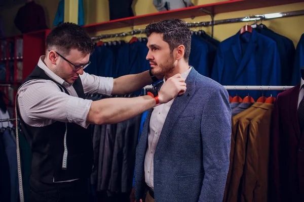 Empresario en chaleco clásico contra los trajes de fila en la tienda. El hombre ayuda a probar otro traje en la tienda de ropa — Foto de Stock