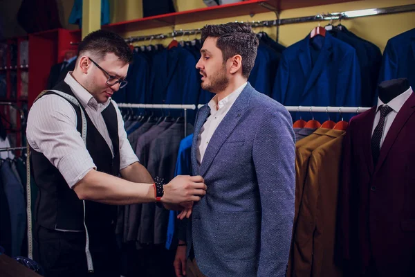 Satır karşı klasik yelek işadamı dükkanda uygun. Adam başka bir takım elbise giyim mağazası denemede yardımcı olur.